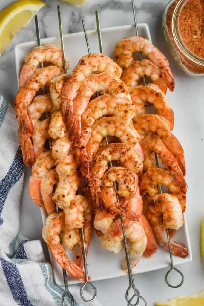 shrimp skewers, seasoned with cajun seasoning in a pile on a white rectangular dish