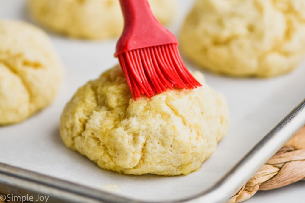 easy biscuit on a parchment lined baking sheet, being brushed with melted butter