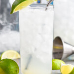 a tall glass with ice filled with a gin rickey, garnished with a lime wedge and with a metal straw