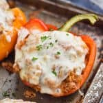 a red bell pepper cut in half and filled with ground turkey, topped with melted provolone cheese and fresh parsley on a rustic baking sheet - 11