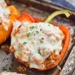 a red bell pepper cut in half and filled with ground turkey, topped with melted provolone cheese and fresh parsley on a rustic baking sheet
