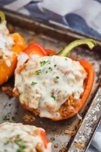 a red bell pepper cut in half and filled with ground turkey, topped with melted provolone cheese and fresh parsley on a rustic baking sheet