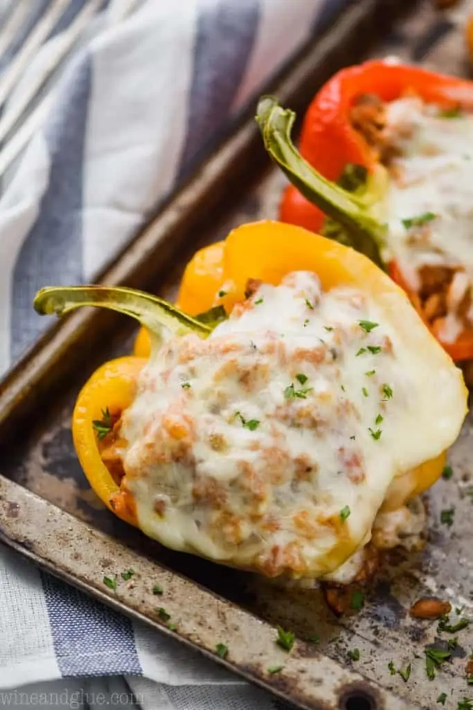 ground turkey stuffed bell pepper with melted cheese and fresh parsley on a baking tray on top of a blue and white striped napkin