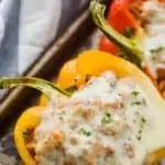 ground turkey stuffed bell pepper with melted cheese and fresh parsley on a baking tray on top of a blue and white striped napkin