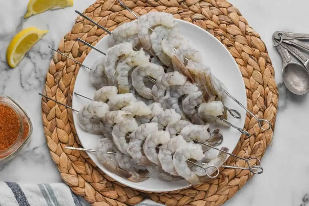 raw shrimp on skewers on a white plate