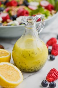 vinaigrette bottle surrounded by cut lemons, fresh raspberries and blueberries and filled with lemon poppy seed salad dressing