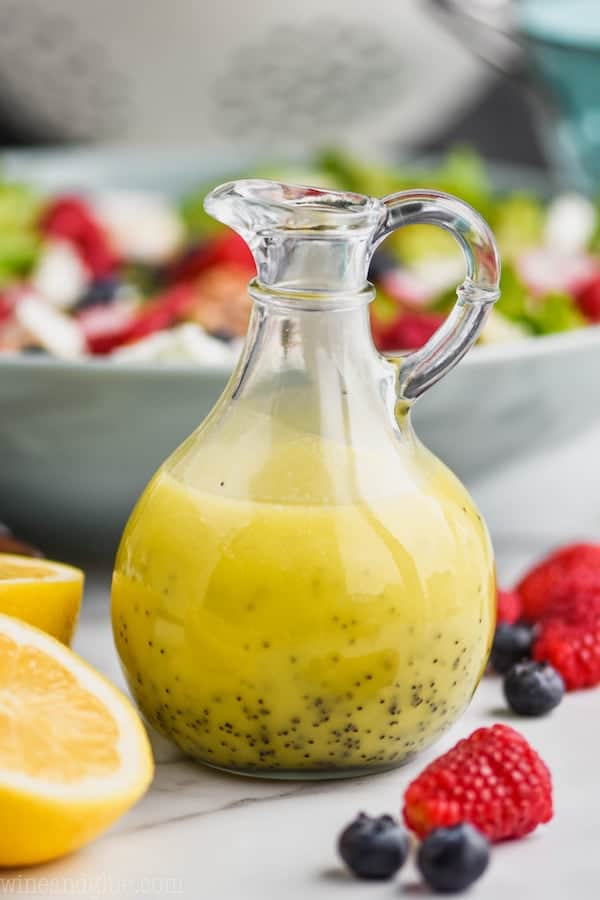 vinaigrette bottle surrounded by cut lemons, fresh raspberries and blueberries and filled with lemon poppy seed salad dressing