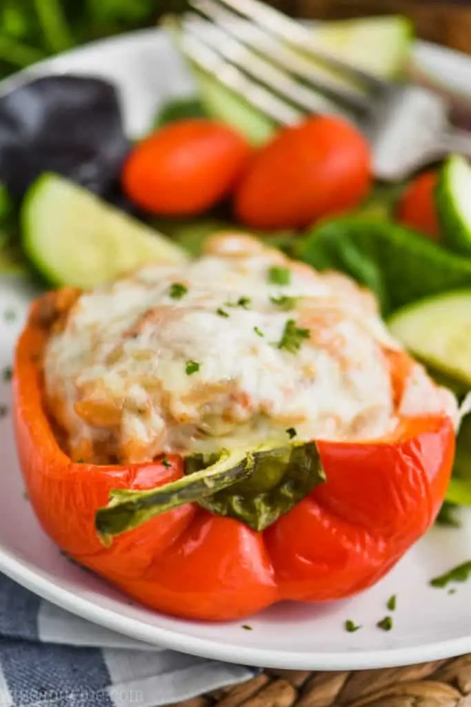 red bell pepper cut in half and stuffed with ground turkey, topped with provolone cheese and fresh parsley on a plate with salad