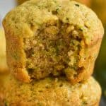 a zucchini muffin that is missing a bites stacked on top of another zucchini muffin with a red and white cloth napkin visible on a gray surface