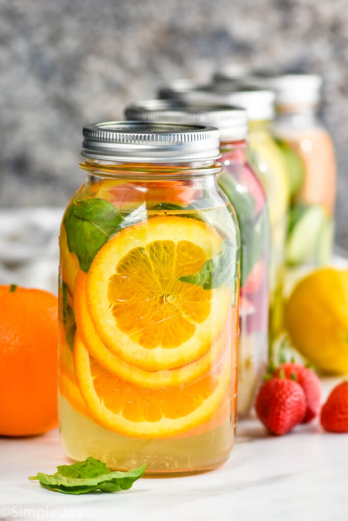 four mason jars lined up with different fruit and herbs in them to make infused water recipes