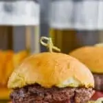 front view of a hamburger made with hamburger seasoning recipe, garnished with red onion, tomato, and lettuce on a bun with beers in the background and fries in the foreground