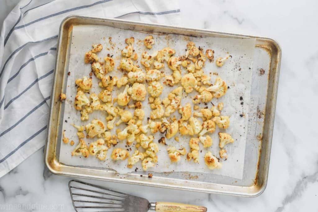 overhead view of roasted cauliflower recipe on a baking sheet that is lined with parchment paper, on a marble countertop with a striped kitchen towel underneath the baking sheet