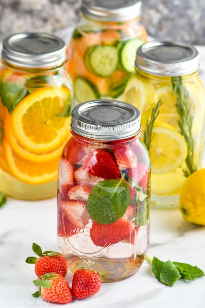 four mason jars filled with fruit and fresh herbs to make infused water