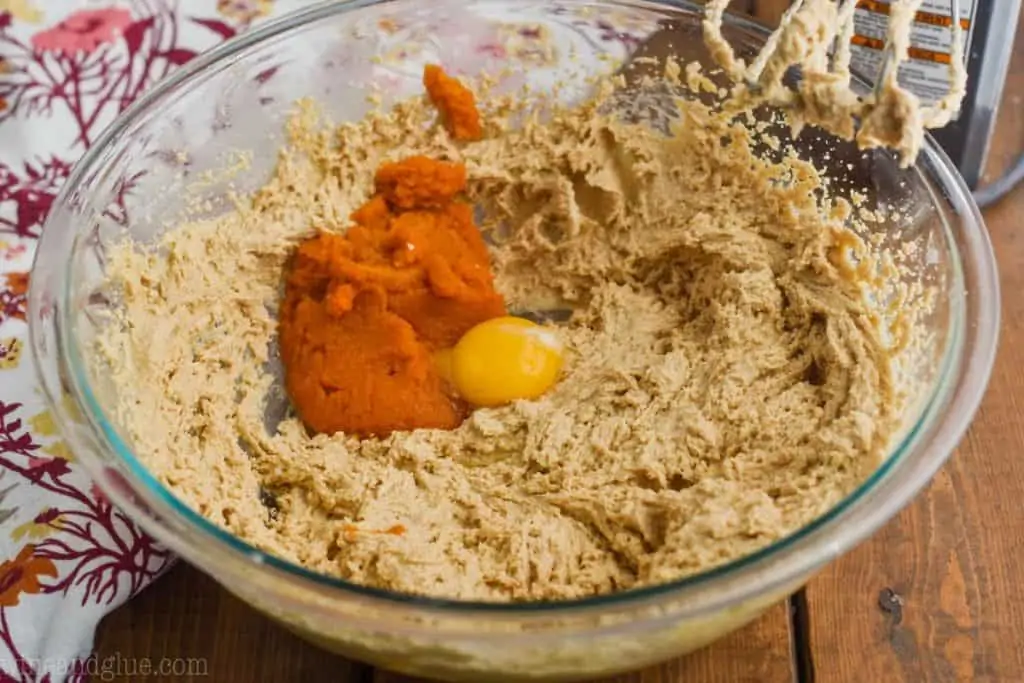pumpkin puree and an egg yolk being added to pumpkin peanut butter cookie batter in a large glass bowl - 4