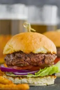 up close of a hamburger made with the best hamburger seasoning, garnished with red onion, tomatoes, and lettuce on a bun held by a toothpick