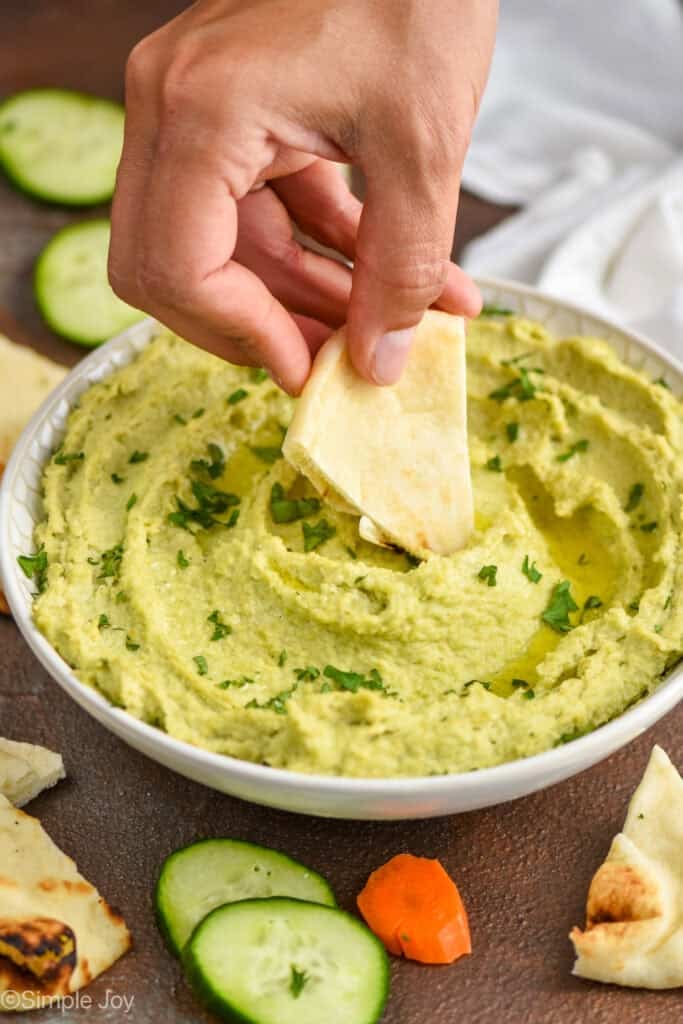 woman dipping a wedge of naan bread into a edamame hummus bowl