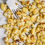 overhead view of roasted cauliflower on a parchment lined baking sheet, being dished up by a slotted spatula - 10