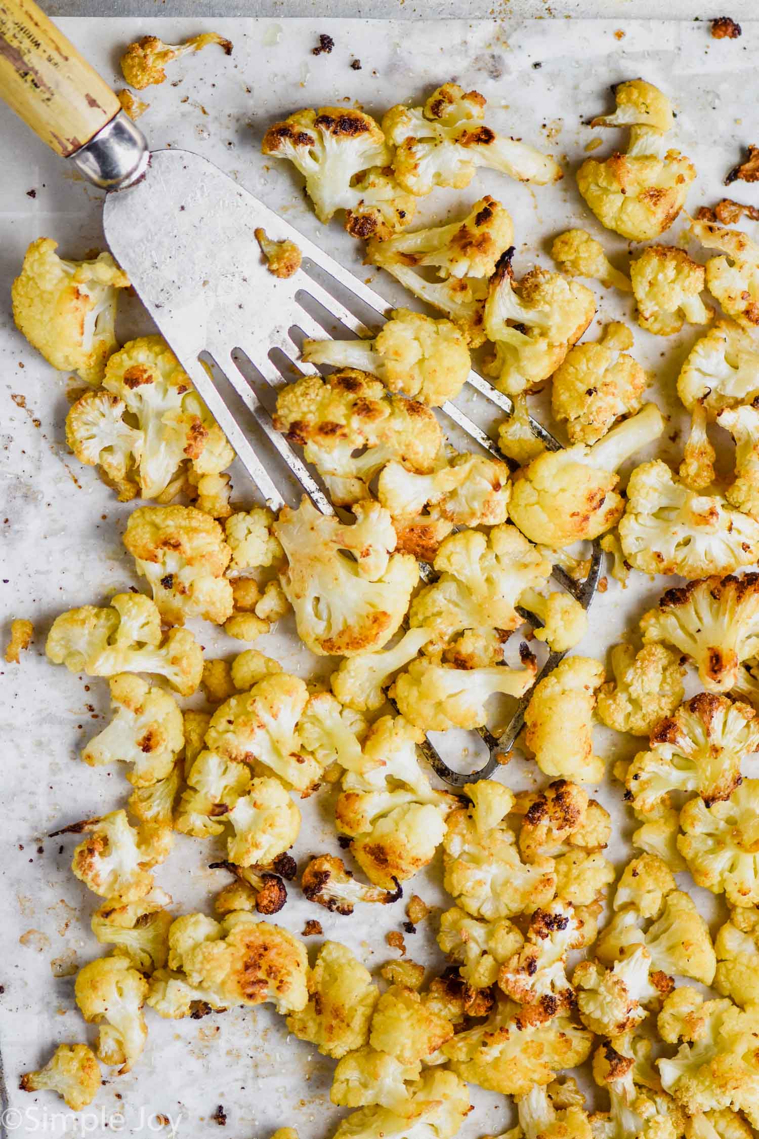 overhead view of roasted cauliflower on a parchment lined baking sheet, being dished up by a slotted spatula