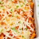 close up of a pan of baked ziti in a white ceramic dish, garnished with parsley