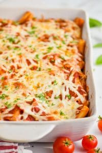 close up of a pan of baked ziti in a white ceramic dish, garnished with parsley