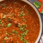 overhead view of a red stock pot filled with vegetarian chili and garnished with cilantro on a black surface top