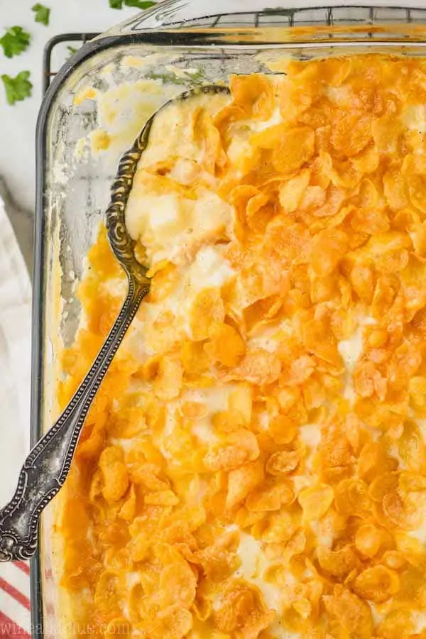 overhead view of a clear baking dish filled with cheesy potatoes with corn flakes with a spoon going into it