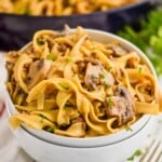 two stacked white bowls with the top one full of ground beef stroganoff recipe - egg noodles, mushrooms, parsley, and a skillet with the rest of the recipe in the background - 17