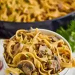 two stacked white bowls with the top one full of ground beef stroganoff recipe - egg noodles, mushrooms, parsley, and a skillet with the rest of the recipe in the background
