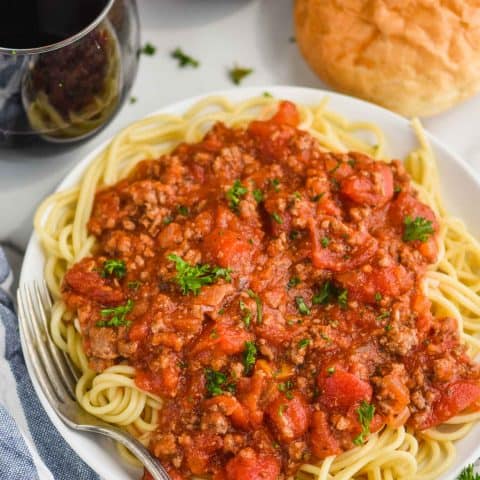 overhead view of a white plate with spaghetti and homemade spaghetti meat sauce, two glass of red wine and french bread