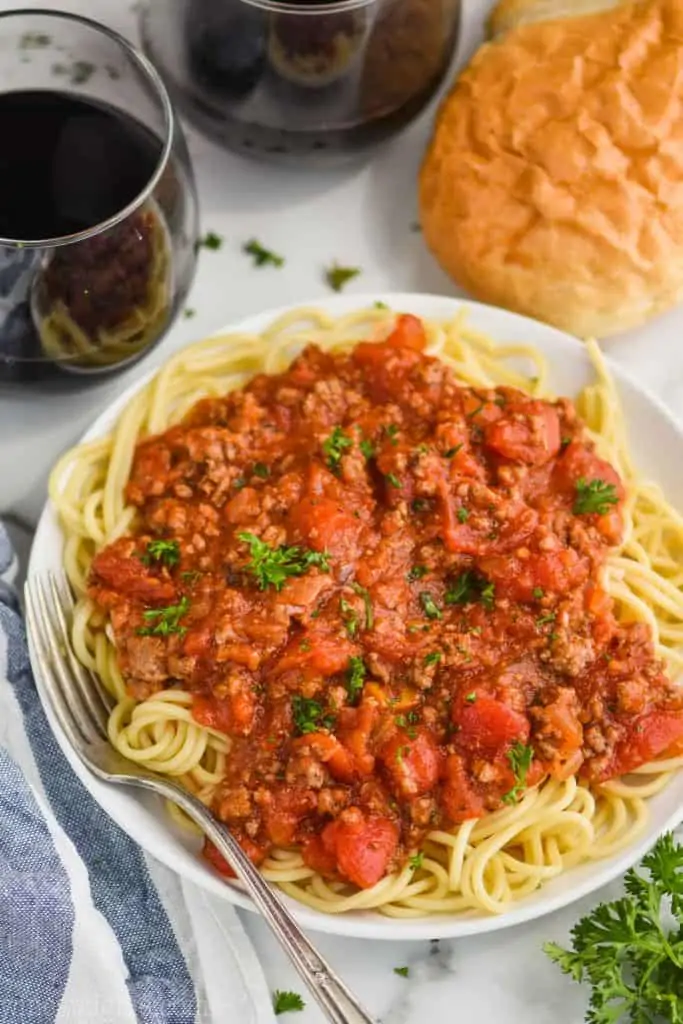 overhead view of a white plate with spaghetti and homemade spaghetti meat sauce, two glass of red wine and french bread