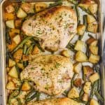 sheet pan chicken recipe consisting of three bone in chicken breasts (nice and browned skin) on a bed of cubed potatoes and green beans on a rimmed baking sheet on a white marble countertop