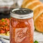 ball jar filled with meat sauce for pasta, with a plate of pasta blurred in the background and a french baguette, parsley in the foreground