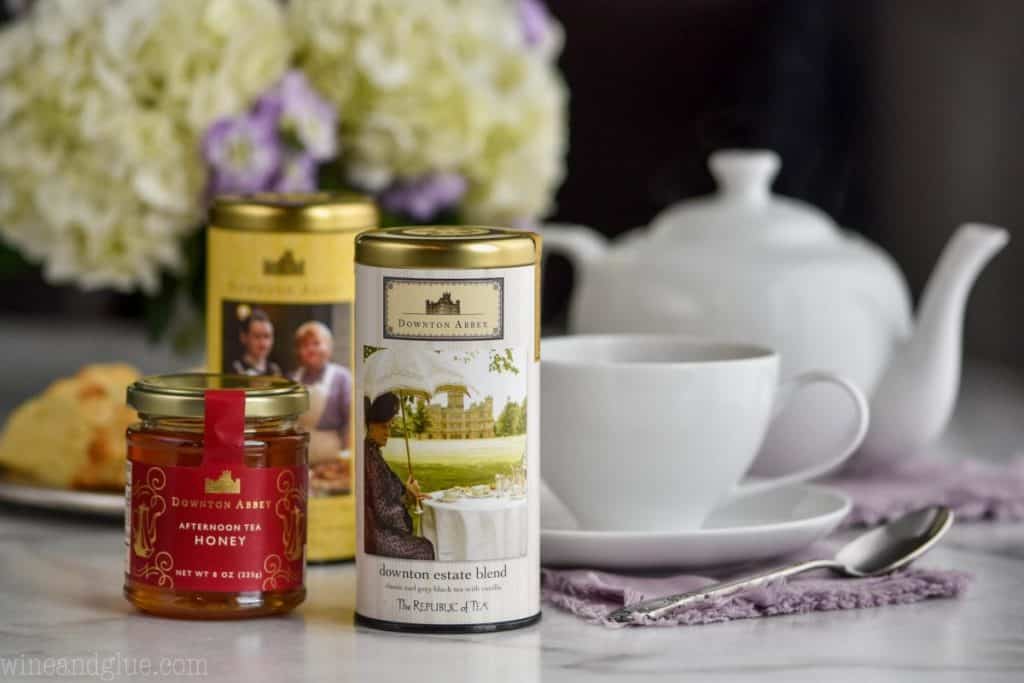 a canister of tea, next to a jar of honey with a tea cup and a tea pot in the background