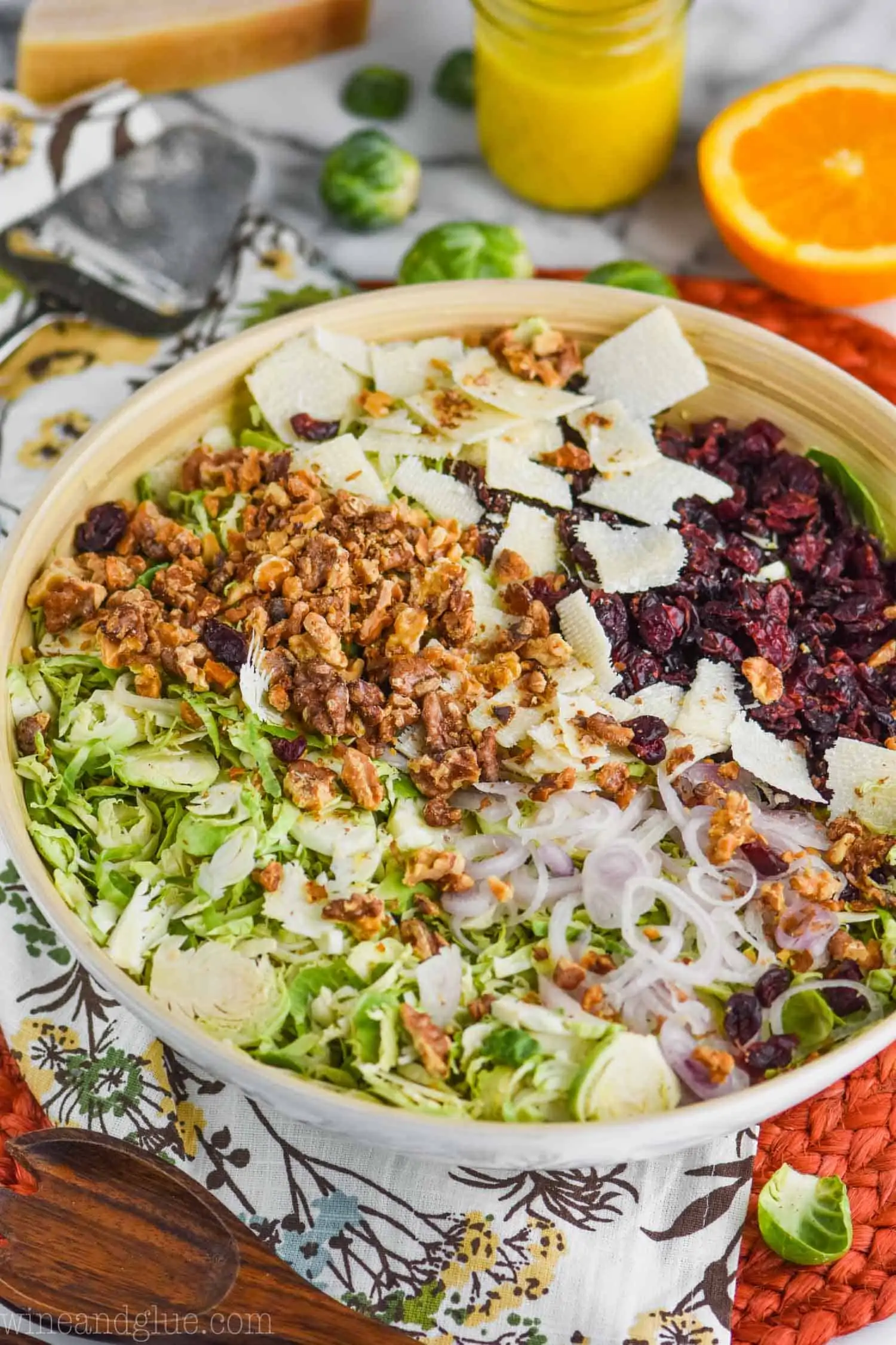 white wooden bowl with brussel sprouts salad with cranberries, shaved parmesan, walnuts and thinly sliced shallots