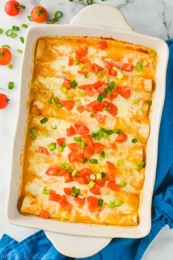 overhead view of white ceramic baking dish filled with buffalo chicken enchilada recipe that is garnished with green onions and chopped tomatoes