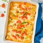 overhead view of white ceramic baking dish filled with buffalo chicken enchilada recipe that is garnished with green onions and chopped tomatoes