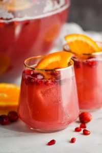 two glasses full of red holiday punch recipe with cranberries floating and orange slices in it