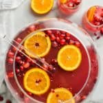 overhead view of sphere punch bowl with non alcoholic Christmas punch with orange slices and cranberries floating in it and two glasses full of it