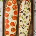 overhead view of two halves of a french bread pizza, one with pepperoni and the other with olives and peppers