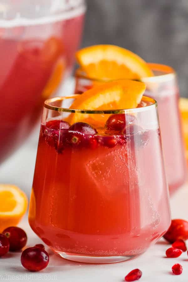 a gold rimmed wine glass full of non alcoholic holiday punch with cranberries floating in it and an orange wedge