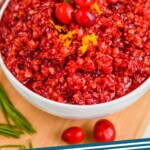 a bowl of cranberry relish recipe with three cranberries, orange zest, and some rosemary on top, says: "cranberry relish simplejoy.com"