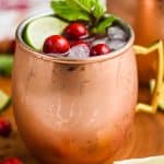 close upon a copper mug that is full to the brim with cranberry moscow mule, garnished with fresh cranberries, a lime wedge, and a sprig of fresh mint