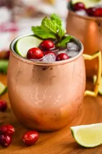 close upon a copper mug that is full to the brim with cranberry moscow mule, garnished with fresh cranberries, a lime wedge, and a sprig of fresh mint