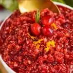 up close picture of a white bowl full of cranberry relish being spooned up by a golden spoon