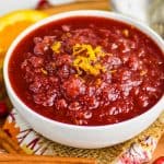 cranberry sauce in a white bowl with orange zest on top, sitting on a pieces of burlap and a fall napkin with cinnamon sticks and fresh cranberries around - 7