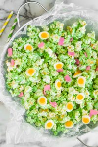 overhead view of popcorn coated in green chocolate in a large metal tray with candy eggs and candy ham to make green eggs and ham popcorn