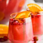two glasses full of red holiday punch recipe with cranberries floating and orange slices in it - 9