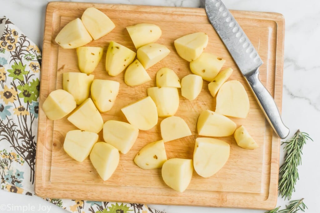overhead of a wooden cutting board with potatoes that have been peeled and quartered