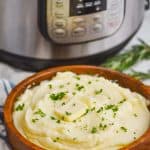 mashed potatoes made in the instant pot in a wooden bowl sitting in front of an instant pot, with a cloth napkin next to it