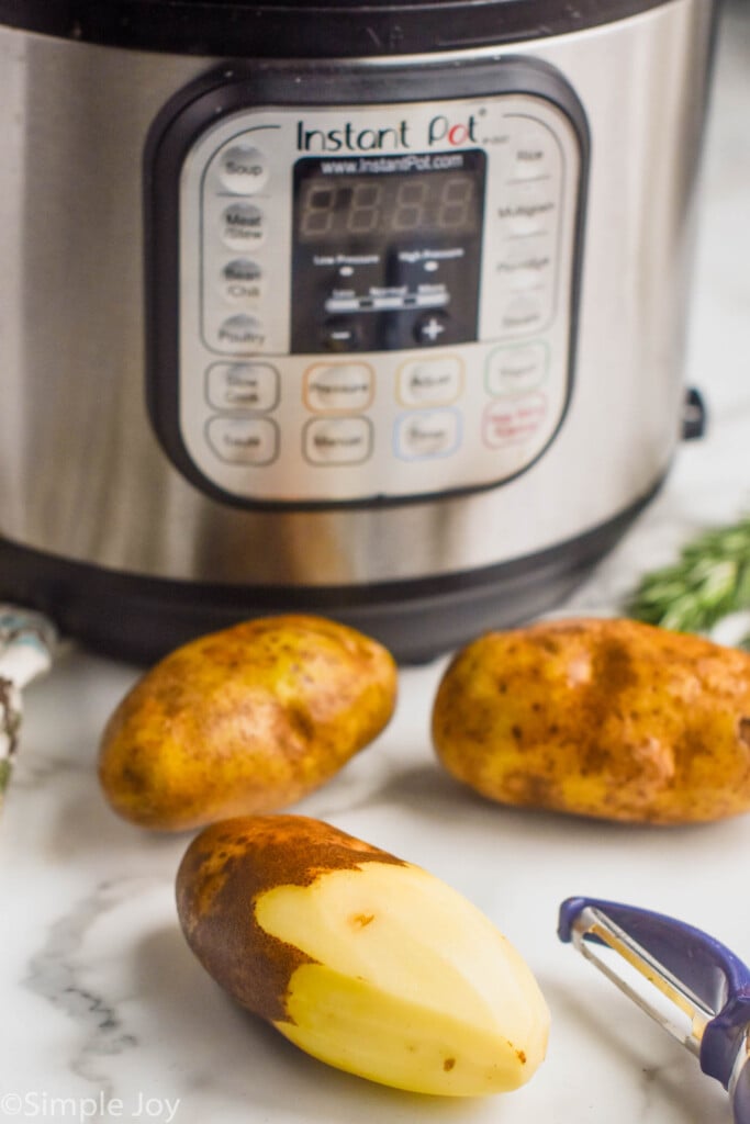 three russet potatoes for creamy mashed potatoes, one half peeled, sitting in front of an instant pot
